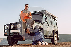 Young man traveler drinking from his thermocup while halt on a hike