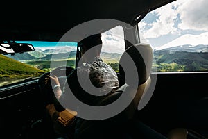 Young Man Traveler Driving A Car In The Mountains In Summer, Rear View From The Car