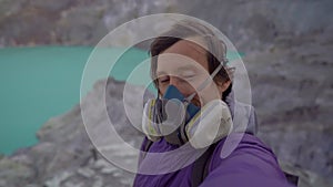 Young man traveler shoots a selfie video in the crater of the Ijen volcano or Kawah Ijen with a big acid lake in it