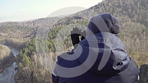 Young man traveler sitting on the rock mountain peak looking with binoculars 4k