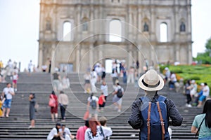 Young man traveling backpacker with hat, Asian hipster traveler looking to Ruins of St. Paul`s, Historic Centre of Macau, a UNESC