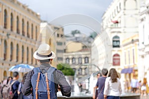 Young man traveling backpacker with hat, Asian hipster traveler standing on Senado Square, landmark and popular for tourist attrac