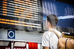 Young man traveling, reading train timetable in railway station