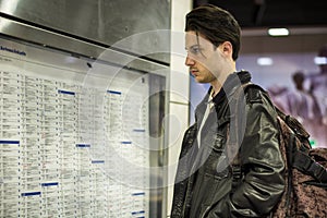 Young man traveling, reading train timetable in railway station