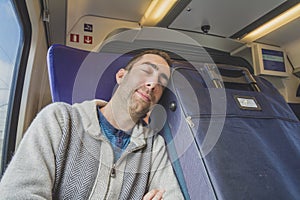 Young man traveling on a train and sleep on blue suitcase next t