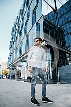 A young man travels through the streets of the city. Boy in sunglasses Stylish man near the building. The man sits on a
