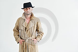 Young man in a trench coat and hat over white background with copy space