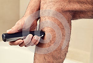 Young man trimming his legs with an electric trimmer