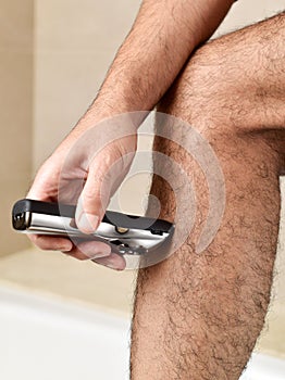 Young man trimming his legs with an electric trimmer