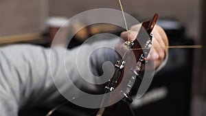 A young man tunes an acoustic guitar plucking the strings and musical notes