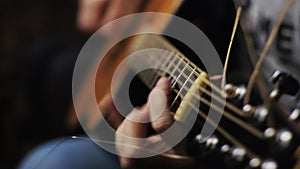 A young man tunes an acoustic guitar plucking the strings and musical notes