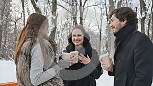 Young man and two girls are drinking coffee and have a good time in winter park