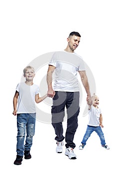 A young man with two small children is walking. Dad, boy and girl in white t-shirts and jeans. Love and tenderness. Full height.