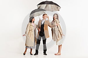 Young man and two women with umbrellas in vintage retro style clothes walking isolated on white background. Timeless