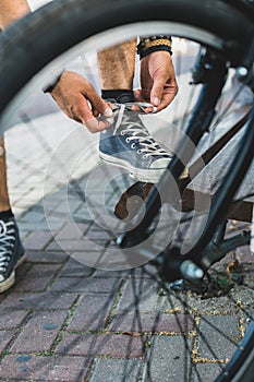 Young man tying his shoelaces before starting daily bike trips, closeup. Lifestyle Activity Footwear Concept