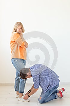 Young man tying shoelaces of his beloved woman posing on the white background. Concept of courtship and reverent