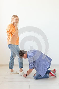Young man tying shoelaces of his beloved woman posing on the white background. Concept of courtship and reverent
