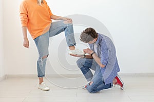 Young man tying shoelaces of his beloved woman posing on the white background. Concept of courtship and reverent