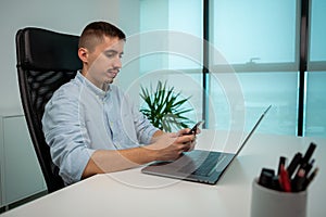 A young man is typing on his smartphone in the office. He is texting