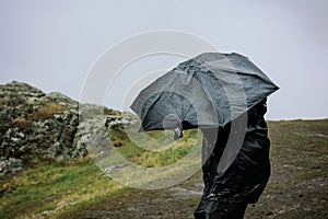 young man under an umbrella in heavy rain and wind on the mountain Azeula Fortress, Kojori, Georgia