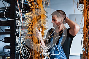 Young man in uniform feels confused and looking for a solution with internet equipment and wires in server room