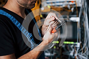 Young man in uniform works with internet equipment and wires in server room