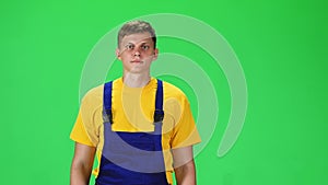 Young man in uniform, yellow t-shirt and blue jumpsuit going and looking forward against green background. Slow motion.