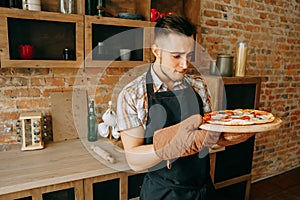 Young man unskilled cook look at self-cooked pizza photo