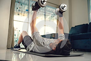 Young man use dumbbell exercises chest fly on yoga mat in living room at home. Fitness, workout and traning at home concept