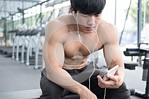 young man use mobile phone in fitness center. male athlete listen to music in cellphone in gym. sporty guy resting in health club