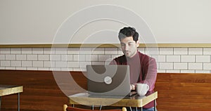 Young man uses a laptop sitting at a small table in a cafe, working remotely