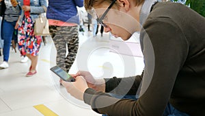 A young man uses a mobile phone in a shopping center.