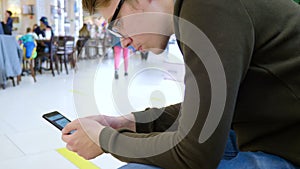 A young man uses a mobile phone in a shopping center.