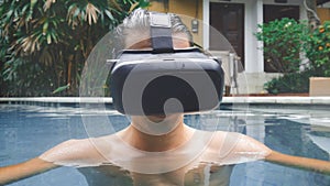 Young man uses virtual reality glasses while swimming in the pool. Guy getting experience in using VR-headset at summer