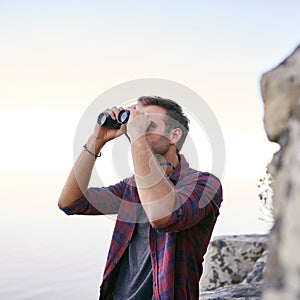 Young man using binoculars outdoors for birdwatching