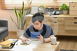 Young man using calculating money bank loan and managing expenses finances in living room. Household finance concept