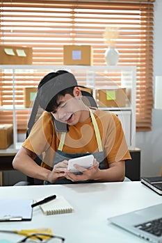 Young man using calculator and confirming orders from customer on mobile phone.