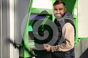 Young man using cash machine for money withdrawal outdoors