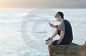 Young man using a cellphone at the beach during sunset.