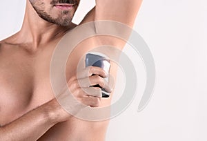 Young man using deodorant on white background, closeup