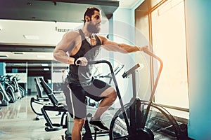 Young man using exercise bike at the gym. Fitness male using air bike for cardio workout at crossfit gym.