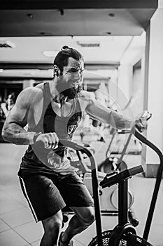 Young man using exercise bike at the gym. Fitness male using air bike for cardio workout at crossfit gym.