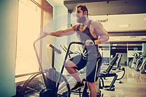 Young man using exercise bike at the gym. Fitness male using air bike for cardio workout at crossfit gym.