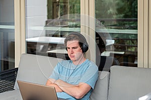 Young man using headphones with laptop computer on outdoor couch