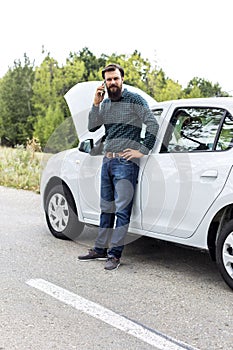 Young man using his cell phone next to a broken down car