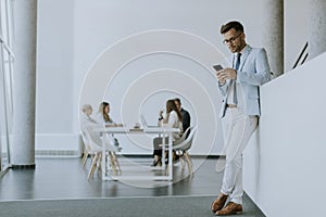 Young man using his mobile phone while his colleagues working in the background