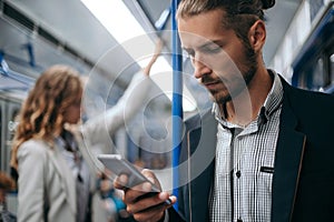 Young man using his smartphone on a subway train.