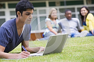 Young man using laptop on campus lawn