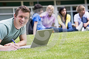 Young man using laptop on campus lawn