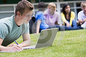 Young man using laptop on campus lawn